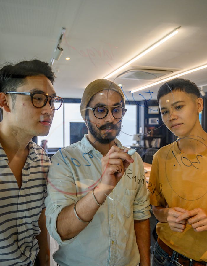 Three colleagues brainstorm ideas on a glass board in a modern office setting.