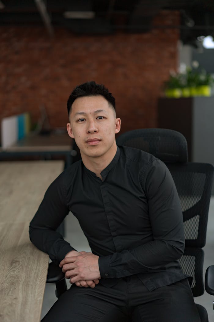 Portrait of a professional Asian man sitting in a modern office setting, exuding confidence and focus.