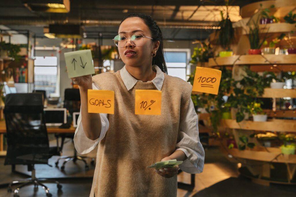 The Art of Drawing Readers In: Your attractive post title goes here Asian woman organizing tasks on sticky notes at modern office workspace.